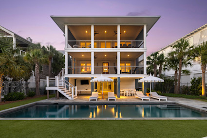 Back house at dusk featuring a patio, a balcony, a fenced in pool, and a yard at 122 Charleston Blvd, Isle of Palms, SC 29451, illustrating the luxury and investment potential of properties in Kiawah Island.