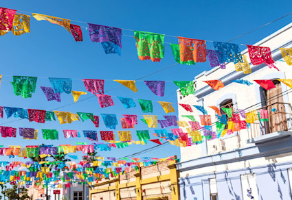 Colorful papel picado hanging above a street against a bright blue sky.