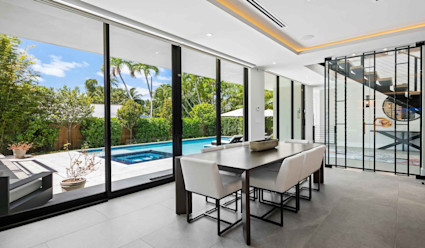 Dining room with small table that seats six with floor to ceiling windows that look out to the pool area. 