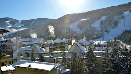 A breathtaking winter view in Vail, Colorado, with snow-covered mountains, alpine-style buildings, ski slopes, and a bright blue sky, encapsulating the allure and exclusivity of elite winter destinations.