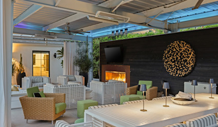 A covered outdoor dining and lounge area with a fireplace.