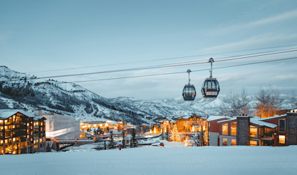 Snowmass resort with several gondolas within view with illuminate lights from the surrounding homes and hotels at dusk with surrounded snowy mountains. 