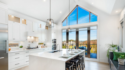 An image of a luxury kitchen with tall ceilings and an autumn scene outdoors.