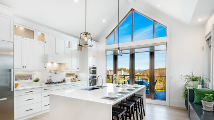 An image of a luxury kitchen with tall ceilings and an autumn scene outdoors.