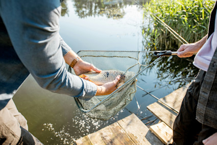 Man holding a fish in a fishing net alongside the water. 