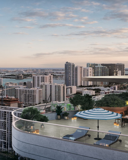 Expansive penthouse terrace with lounge chairs and striped umbrellas overlooking Miami's skyline, bay, and ocean at dusk.