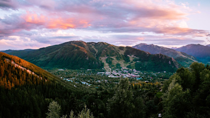 A breathtaking mountain sunset over Aspen, Colorado, with lush spring greenery and the town nestled in the valley below. This visually stunning scene captures the allure and natural beauty of a luxury mountain destination, making it ideal for travelers planning a spring ski getaway.
