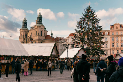 Outdoor holiday market surrounded by gothic buildings with a large Christmas tree at the center.