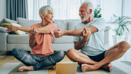 A man and woman know how to make a house a home by stretching on their living room floor in preparation for their online fitness class.