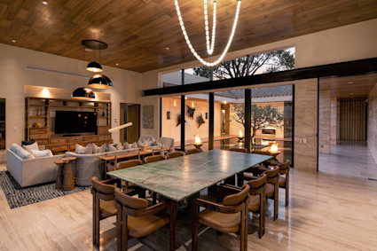 MCB09572__35D4uBOEgVDhXXvk99xwYQ.pngalt textClaude responded: Warm open-plan living and dining space with a green marble table and lounge, opening through glass walls to a fire-lit courtyard at dusk.Warm open-plan living and dining space with a green marble table and lounge, opening through glass walls to a fire-lit courtyard at dusk.
