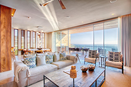 Sun-drenched open-plan living room with floor-to-ceiling windows opening onto an oceanfront terrace.