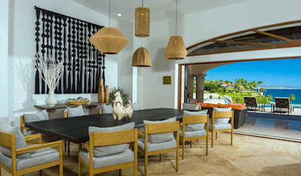 A dining room with dining table and chairs with panoramic doors that open up to the backyard that overlooks the ocean.