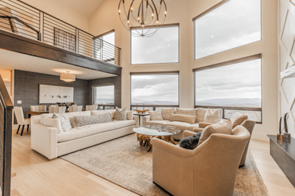 Living room with high ceilings and lots of windows with cream-colored furniture arranged in a circle around a glass coffee table.