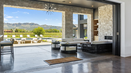 Living area of Napa luxury home looking out from the living area into the covered outdoor area with stonework and pool area with mountain in the background. 