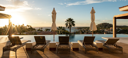 Palmilla outdoor lounge area with lounge chairs placed poolside facing the unobstructed view from the home during a sunset.
