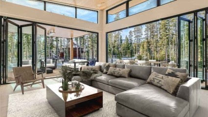 A well-lit living room of a Breckenridge vacation home featuring expansive windows, forest views and a comfortable couch