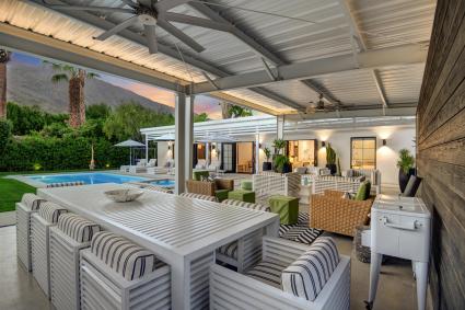 Large covered patio with furniture and tables next to a pool