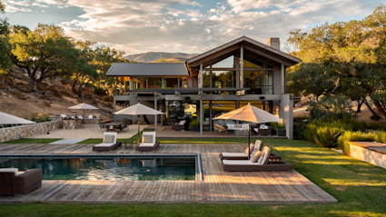 Modern Napa home at golden hour with a pool, sun-loungers, and oak-covered hills rising behind.