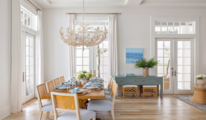 Dining area with a long dining tavle that seats eight with arrangement on the table with a chandelier hanging above that is mean to look like coral.