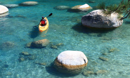 A kayaker paddles through the clear water of Lake Tahoe in summer.