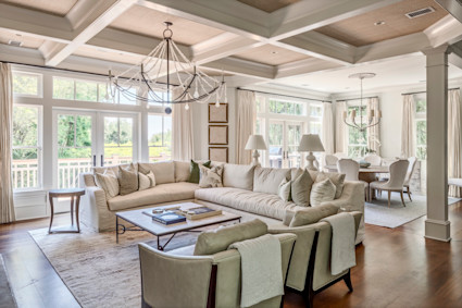 Sun-drenched coastal living room with coffered ceilings, a beaded chandelier and a linen sectional opening to a verdant Kiawah Island view.