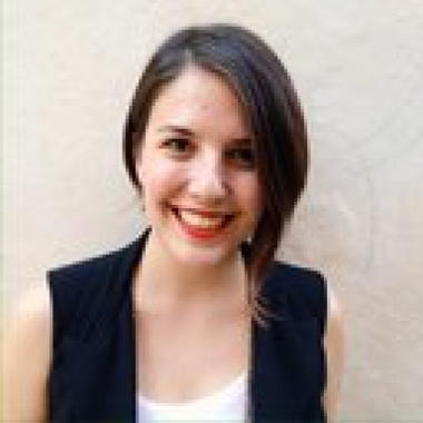 Pe imagine este reprezentată o femeie cu parul brunet, imbractă într-un  maiou alb si vestă neagră. Femeia zâmbește.