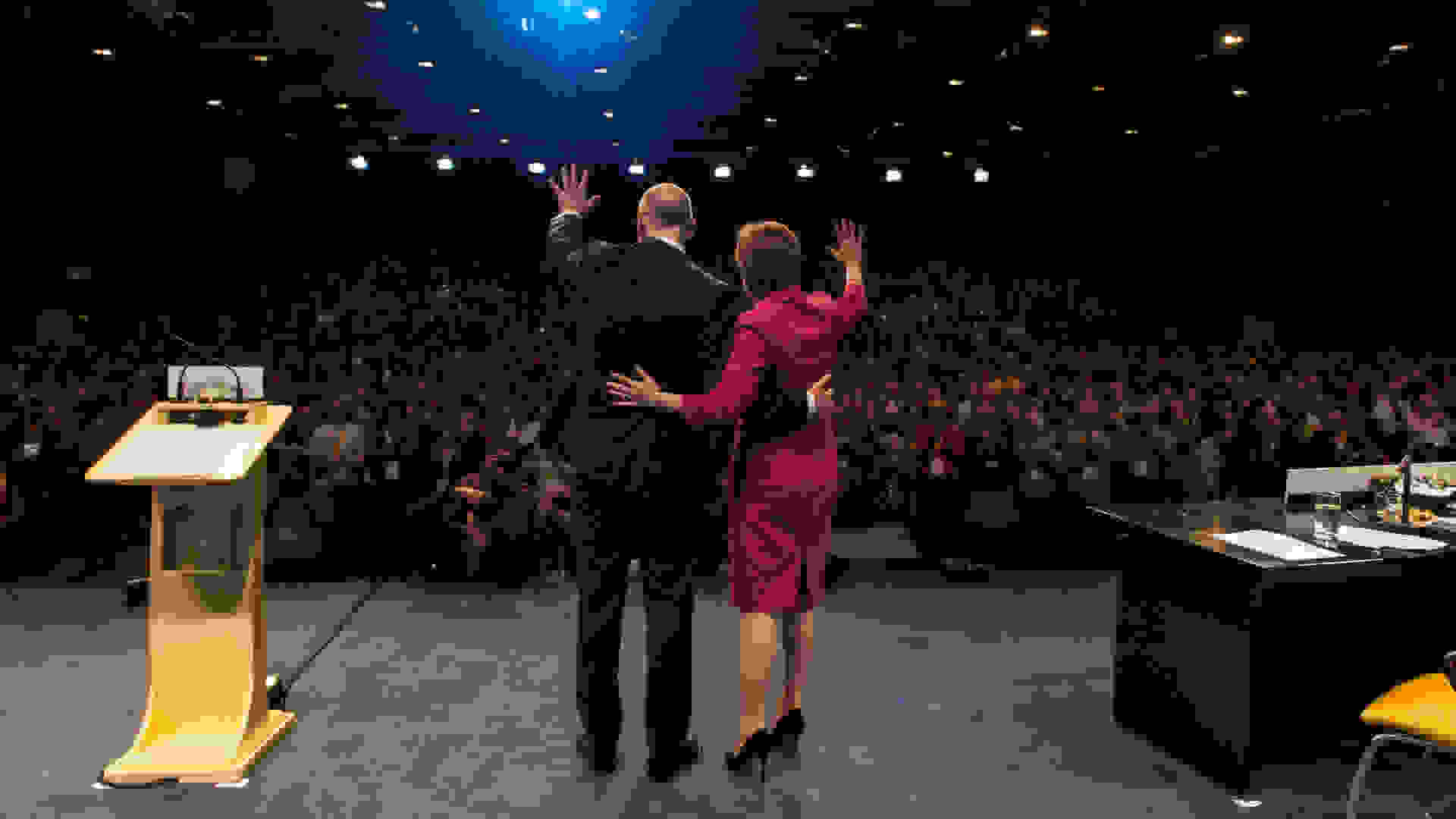 The First Minister of Scotland, Nicola Sturgeon, with Deputy First Minister John Swinney waving to the crowd at the 2015 SNP Conference. Image Courtesy: Ewan McIntosh, Licensed under the Creative Commons Attribution 2.0 Generic