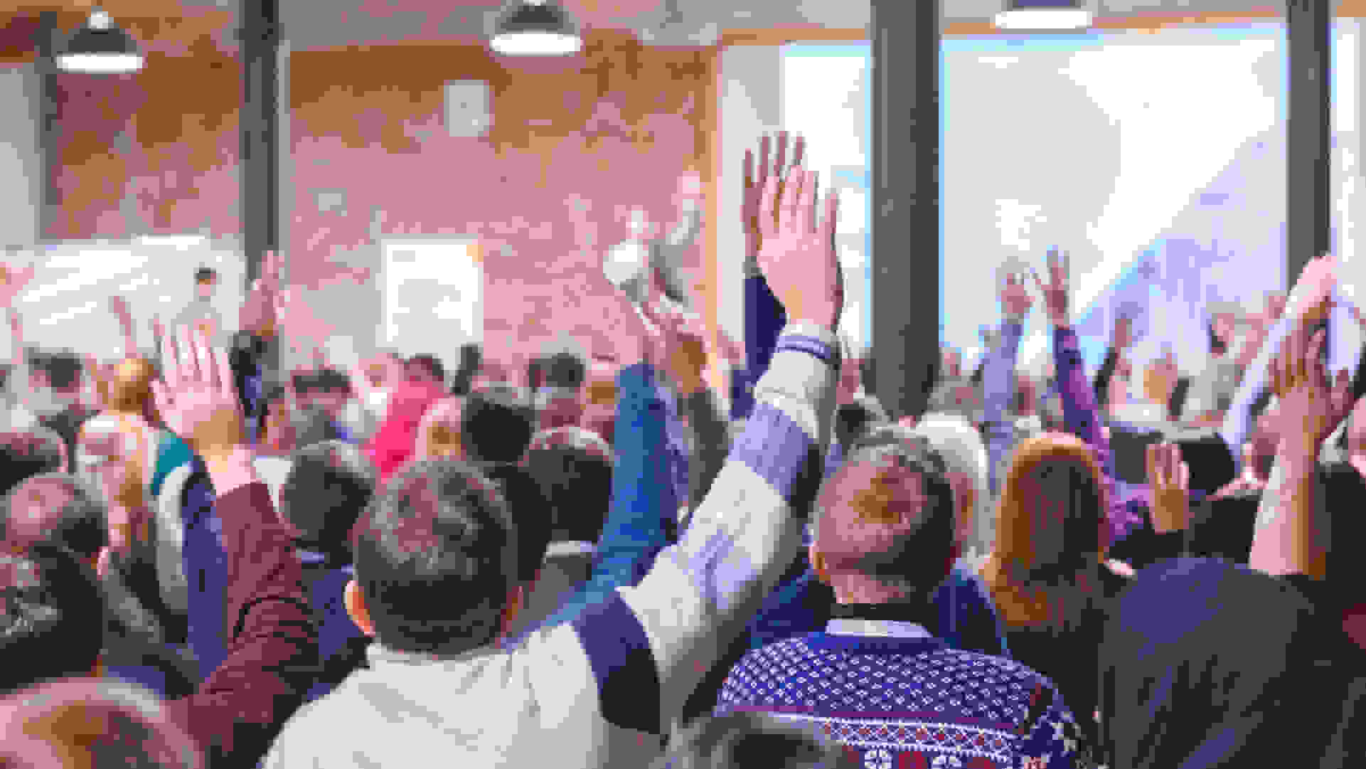 School pupils in an assembly with their hands up.