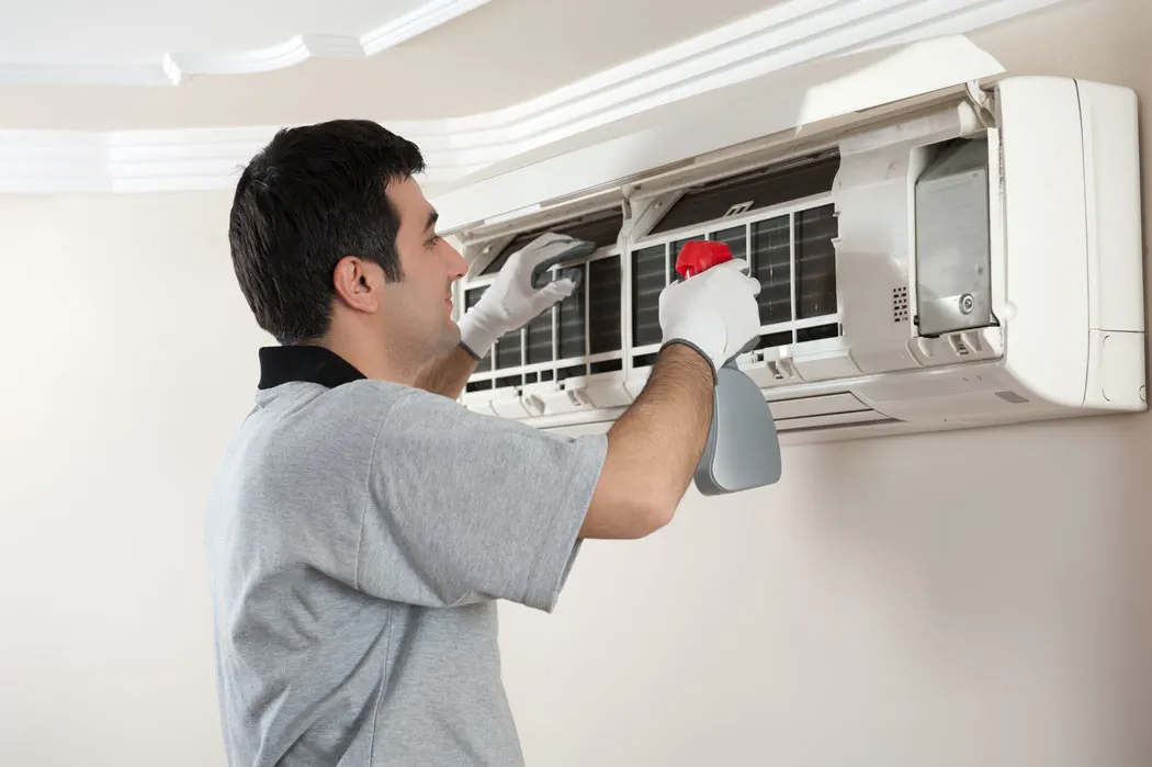 Technician cleaning indoor AC unit. 