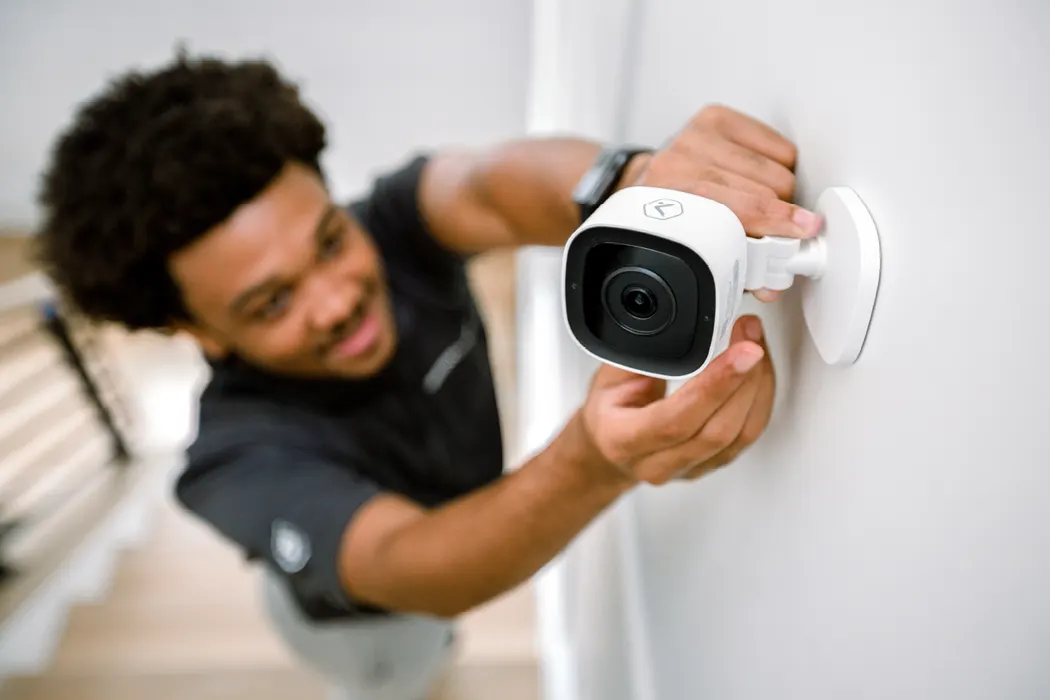 Brinks Home technician placing a wall-mounted ADC Video Camera (image intended for desktop)
