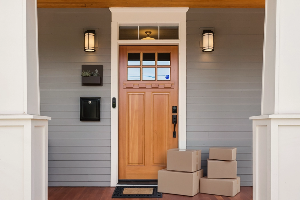A secure front porch setup designed to prevent package theft—featuring a smart doorbell camera, visible security signage, motion-activated lighting, and a smart lock system, with multiple packages placed near the entry.