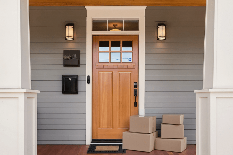 A secure front porch setup designed to prevent package theft—featuring a smart doorbell camera, visible security signage, motion-activated lighting, and a smart lock system, with multiple packages placed near the entry.