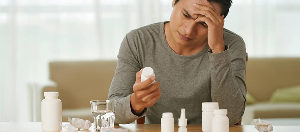Man zit met zijn hoofd in zijn hand aan tafel met potjes medicijnen
