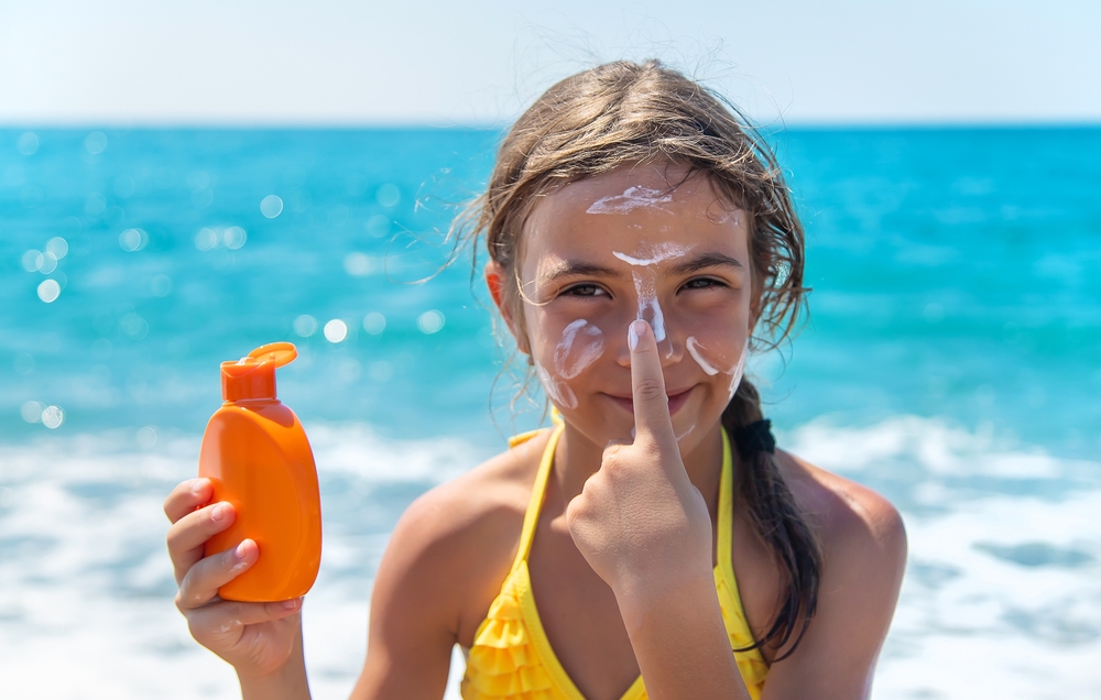 Meisje op het strand smeert zonnebrand op haar gezicht