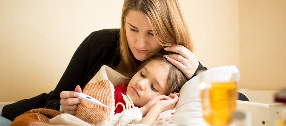 Jongetje met bronchitis ligt ziek op bed met moeder die temperatuur opneemt