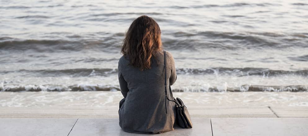 Vrouw kijkt vanaf de boulevard uit  op zee 