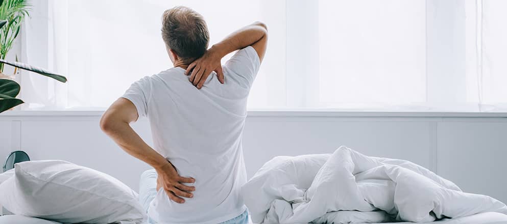 Man zit op bed met last van zijn rug en nek