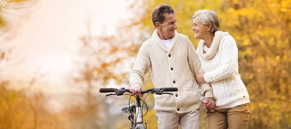Ouder koppel lopen arm in arm door het bos met fiets in de hand