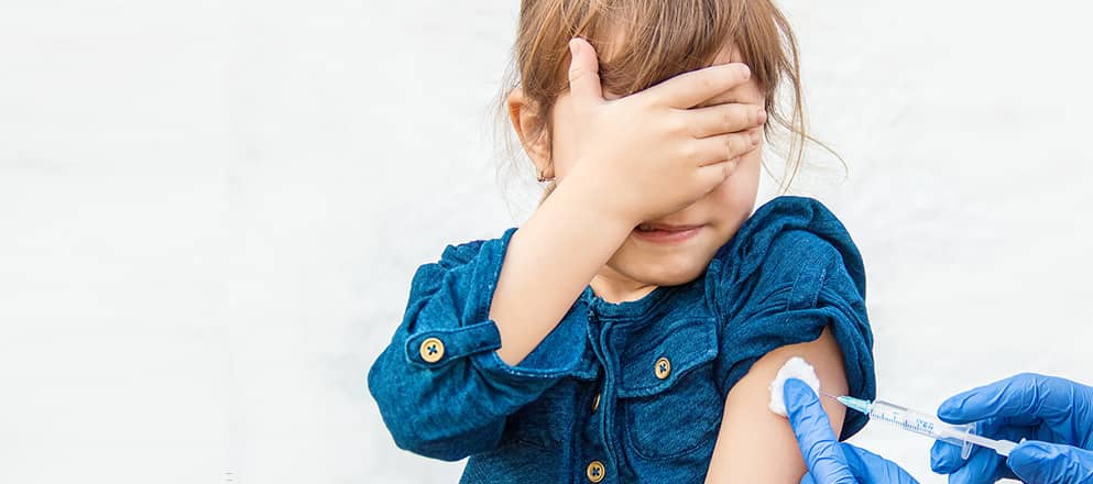 Meisje krijgt een prik in haar arm en houdt hand voor haar ogen