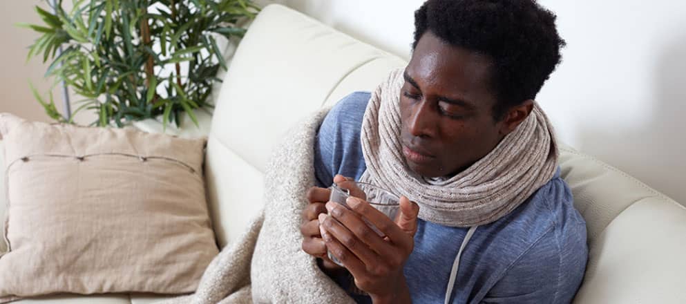 Man zit ineengedoken op de bank met een sjaal gewikkeld in een deken met warme thee