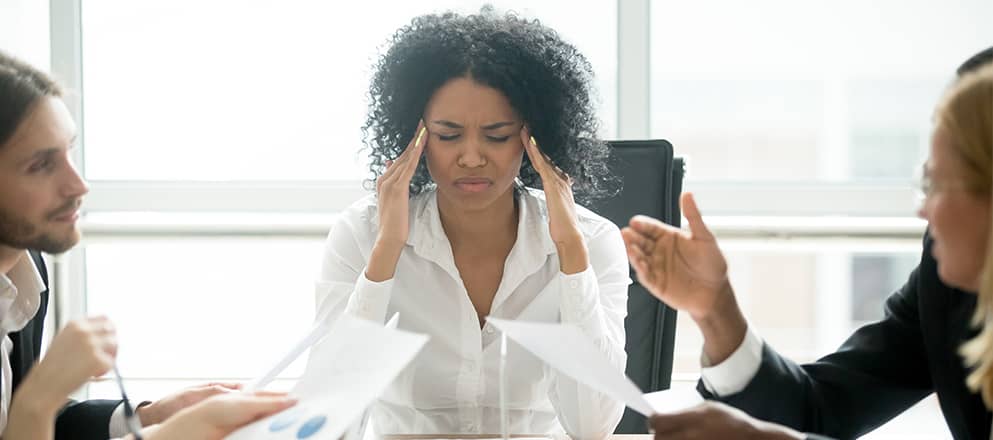 Zakenvrouw zit met haar vingers tegen haar slaap aan, aan de vergadertafel met collega's
