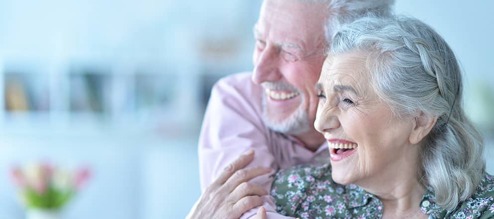 Een oude man en vrouw houden elkaar vast en lachen