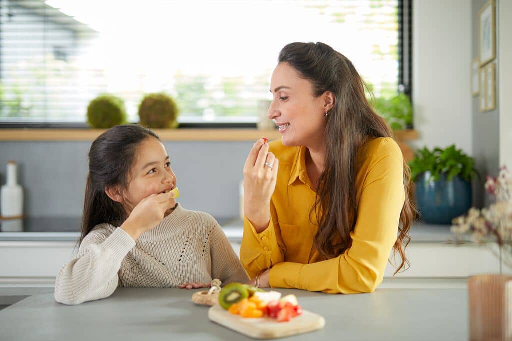 Vrouw en kind een fruit aan de keukentafel.