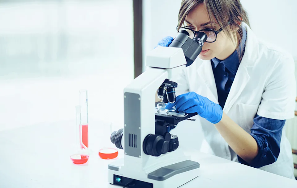 Jeune femme regardant à travers un microscope