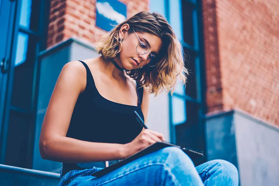 Jeune femme assise sur les escaliers et prenant des notes