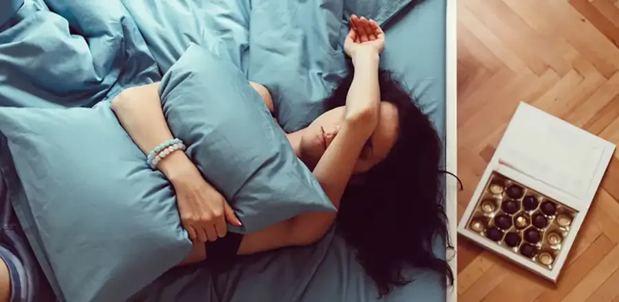 Young woman lying in bed and suffering from stomach pain