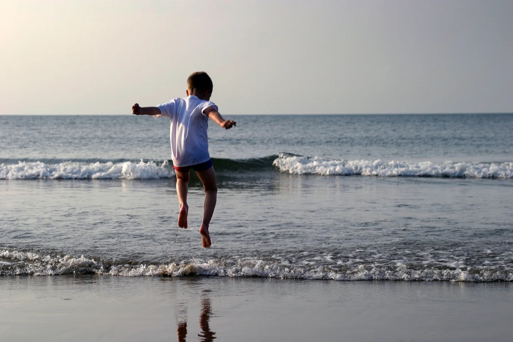 Boy jumping on a beach with small waves