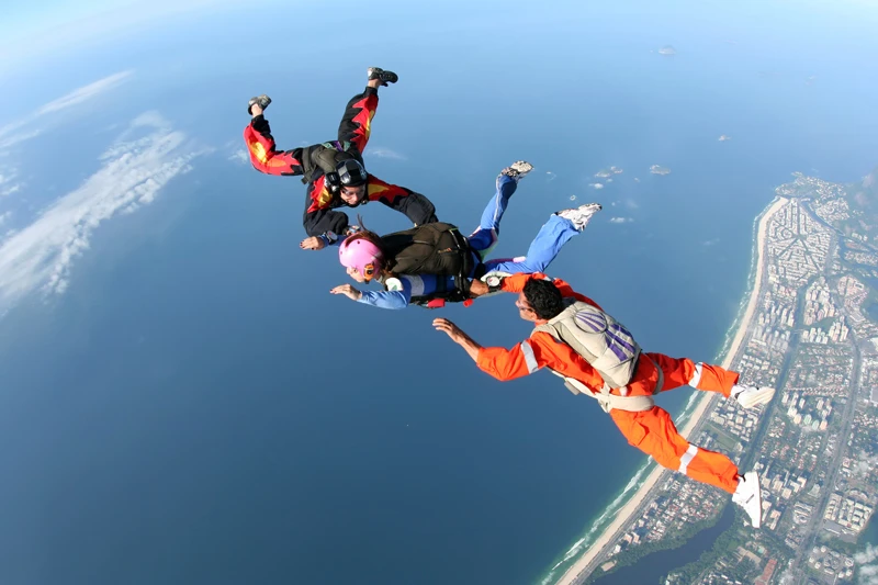 Three skydivers freefalling above a coastal city and ocean