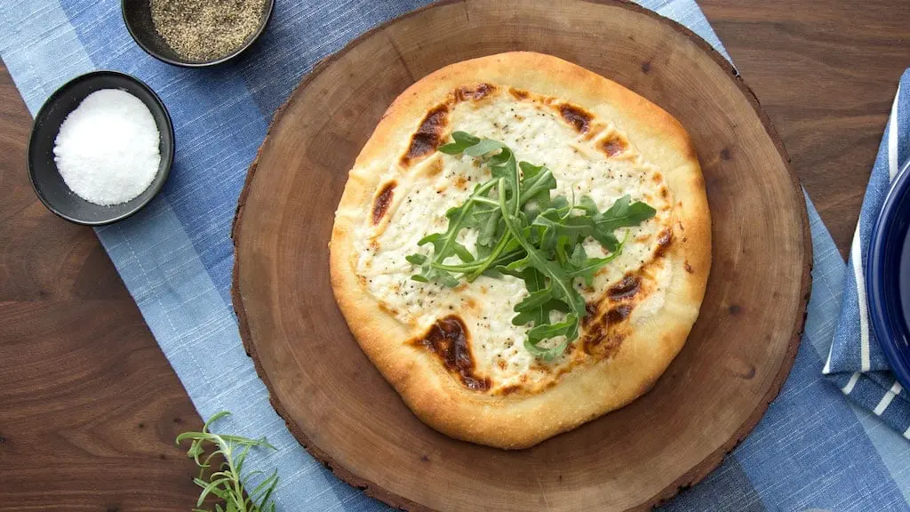 Freshly baked Pizza Bianca topped with creamy ricotta, mozzarella, and a sprinkle of fresh herbs, served on a wooden board for a delicious Italian meal.