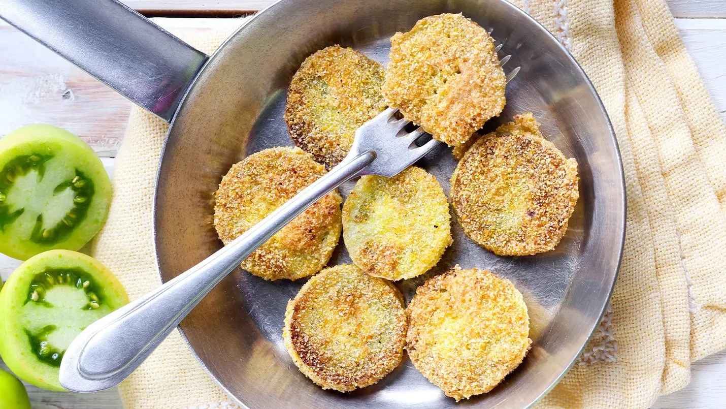 Crispy fried green tomatoes arranged on a plate, served with a creamy dipping sauce and garnished with fresh herbs, perfect for a savory appetizer.
